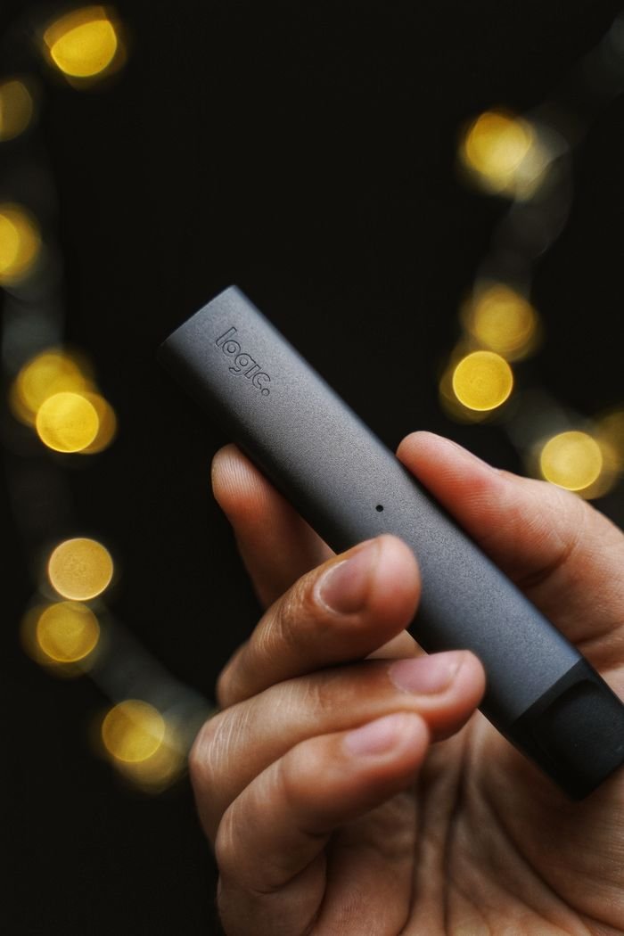 about-02 Detailed shot of a hand holding a sleek e-cigarette with bokeh lights in the background.